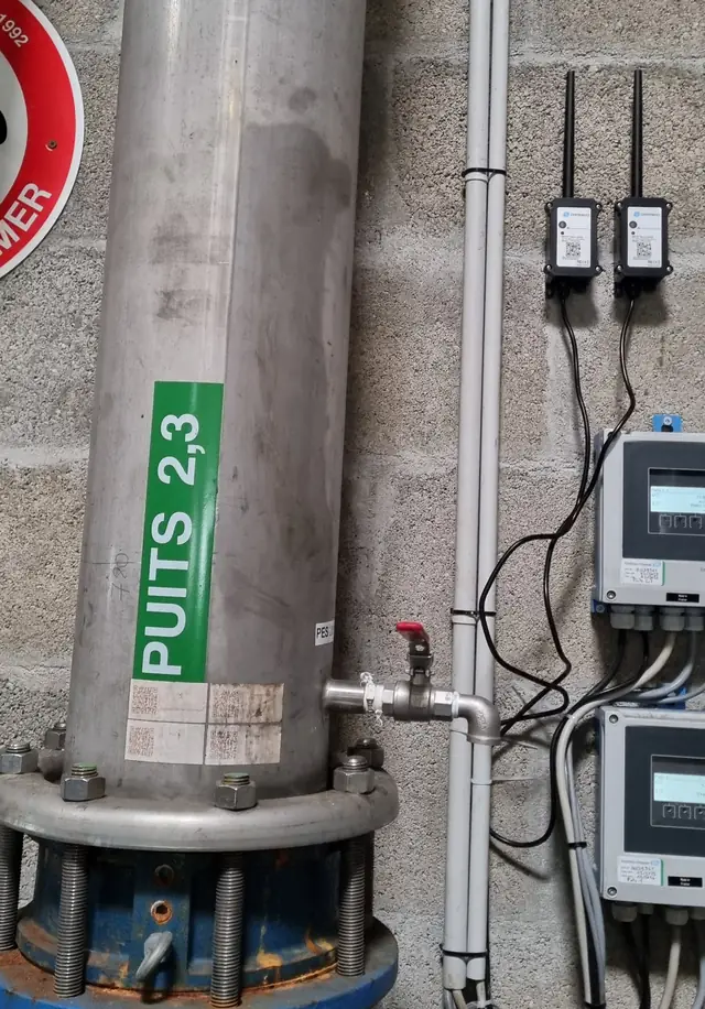 Deux modules Dragino CPL03-CB fixés au mur d'un local de puits, qui comptent les impulsions des débitmètres pour mesurer le débit