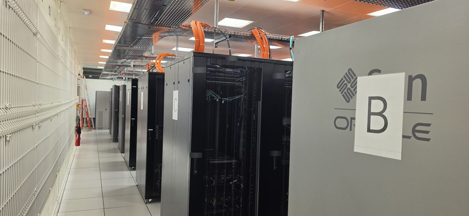 Première salle informatique : rangée de baies noires avec câblage cuivre orange en hauteur