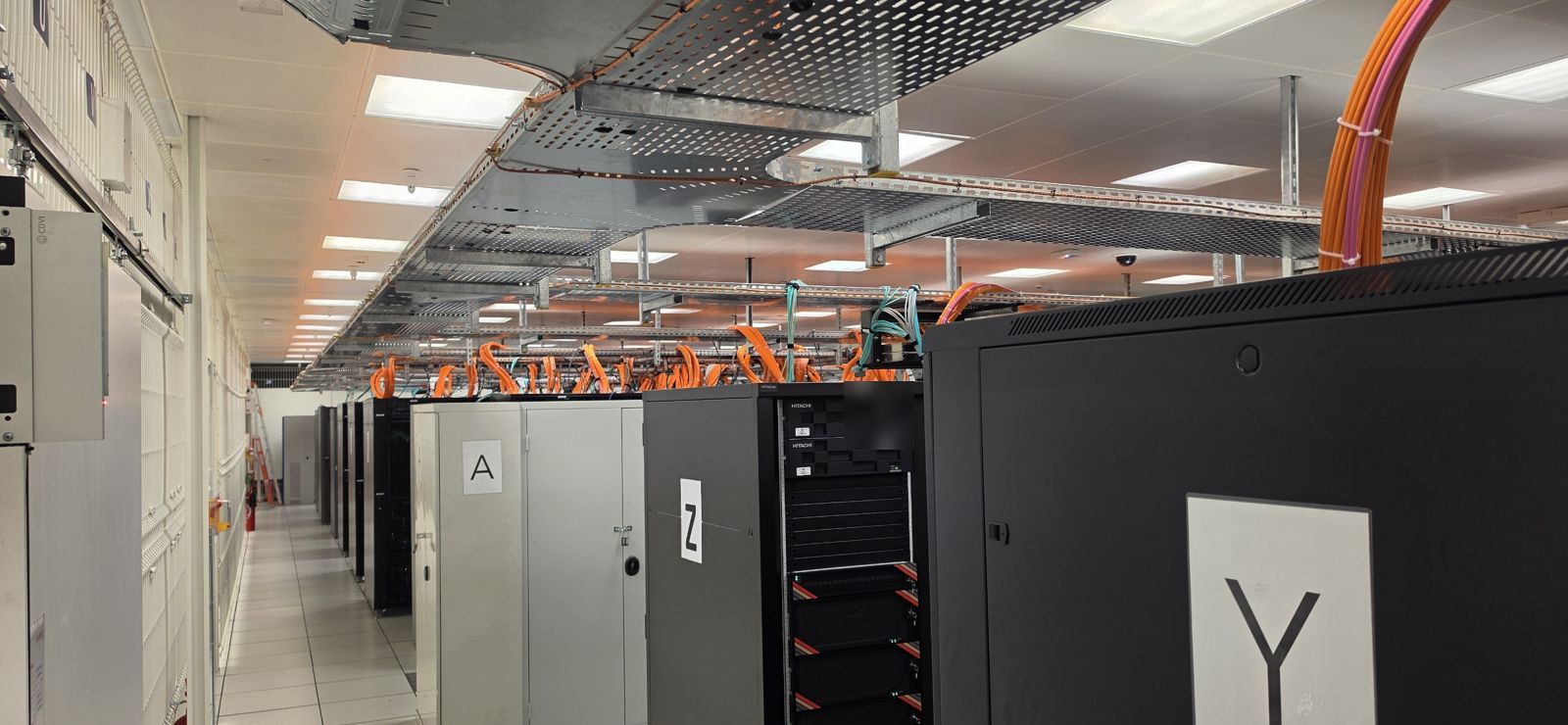 Salle informatique hébergée en datacenter : rangées de baies et chemins de câbles en hauteur